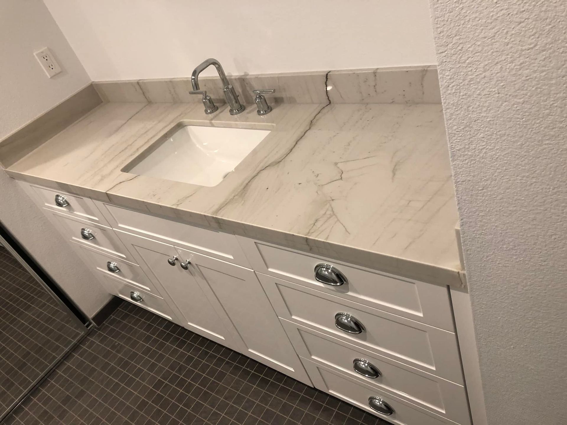 White bathroom vanity with marble-look countertop and sink, chrome faucet, and drawers underneath
