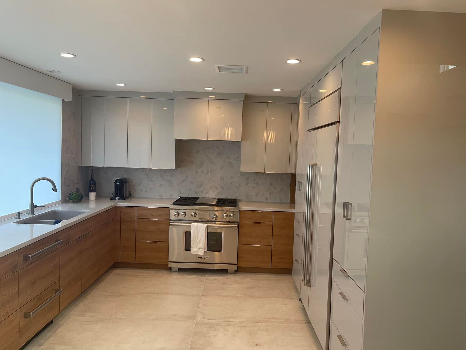 Modern kitchen with light wood cabinets, white countertops, stainless stove, and large window.