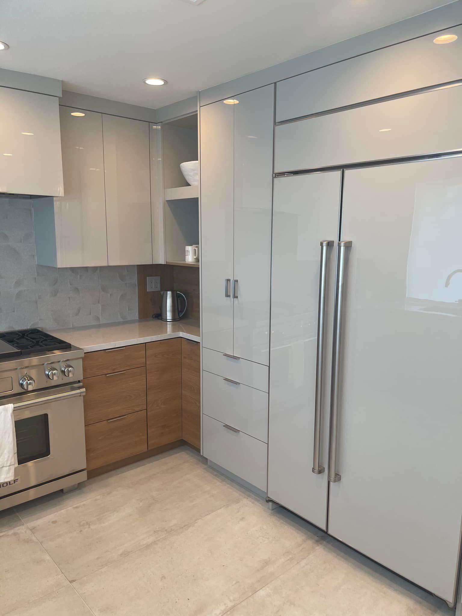 Modern kitchen with glossy white cabinets, stainless steel appliances, and light wood lower drawers