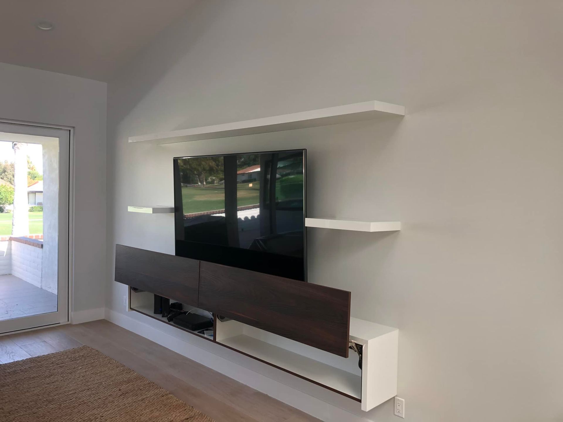 Living room with wall-mounted TV, floating shelves, and a long media console on a light wall