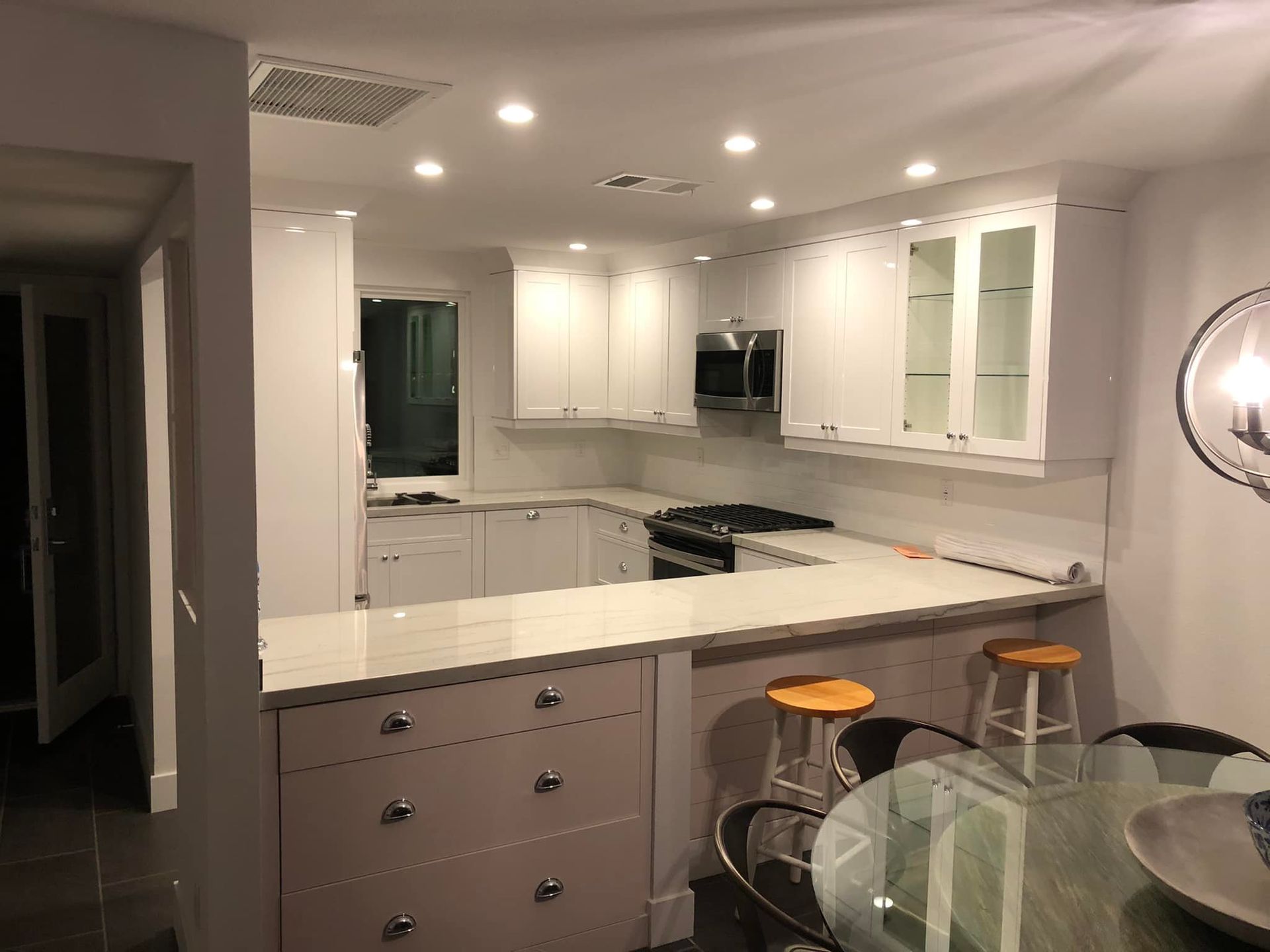 Modern white kitchen with island, pendant lights, bar stools, and glass dining table