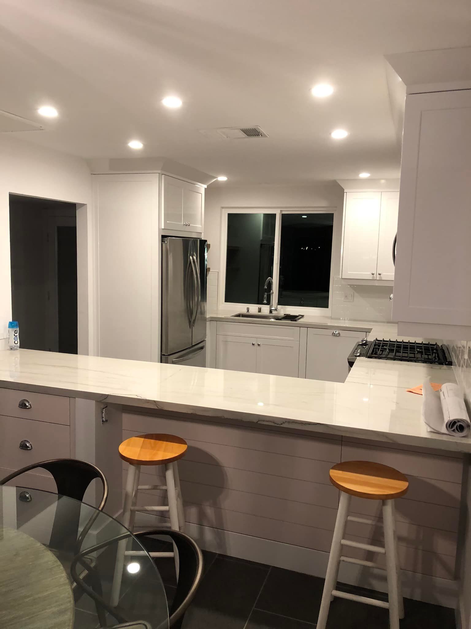 Bright modern kitchen with white cabinets, island stools, and recessed ceiling lights