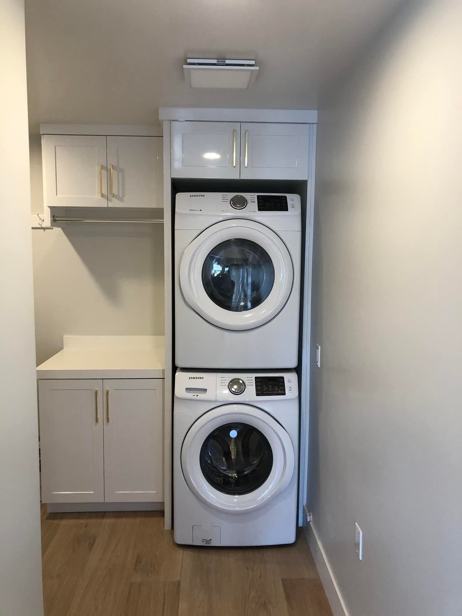 Laundry closet with stacked washer and dryer beside white cabinets in a small room