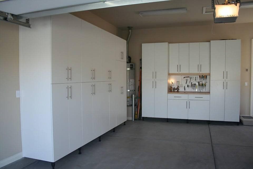 Garage interior with white storage cabinets and built-in workbench along the back wall