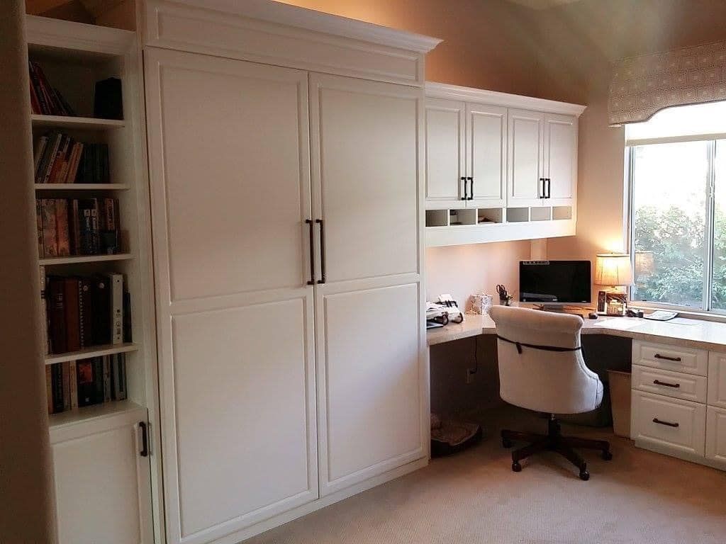 Home office with built-in white cabinets, desk, computer, and a window view.