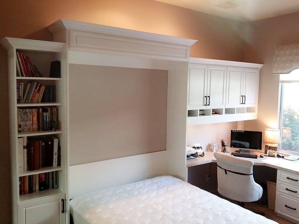 Built-in white desk and shelving nook with a bed tucked underneath in a cozy home office