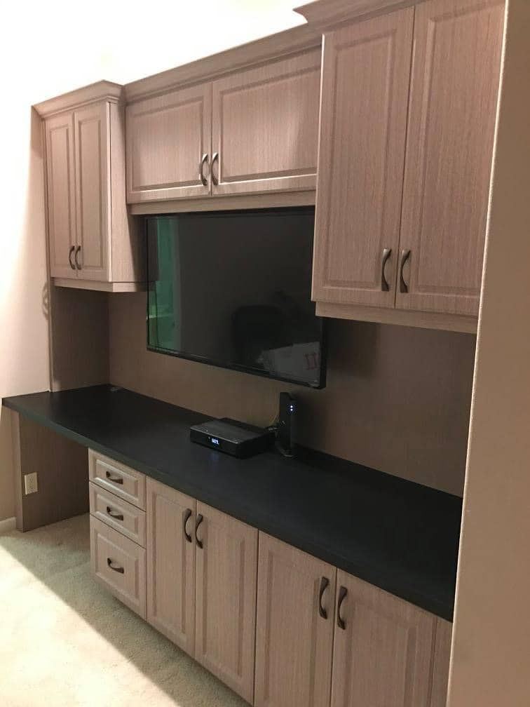Wall-mounted wooden cabinets and black countertop in a small room alcove with a TV screen in the center