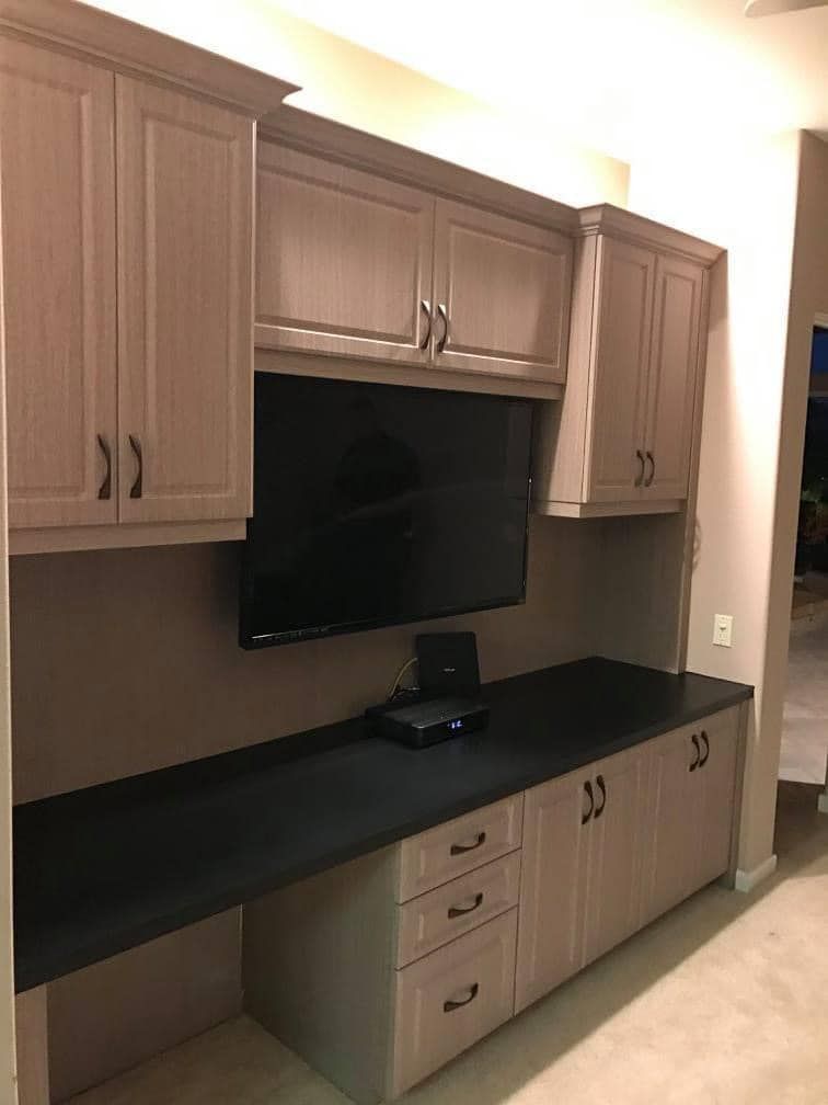 Built-in wooden cabinets and black countertop with wall-mounted TV in a room
