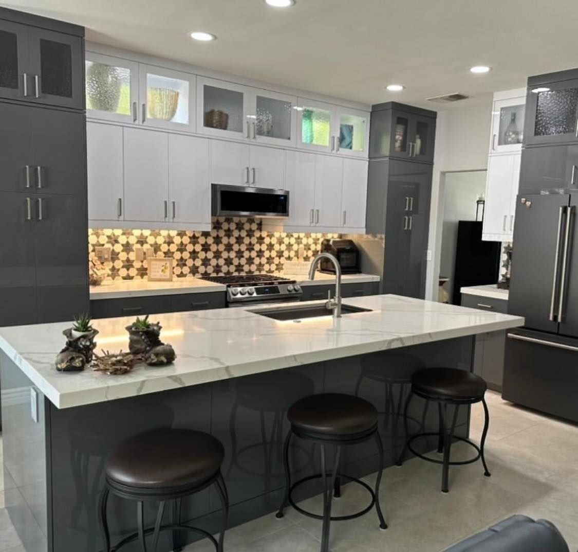 Modern kitchen with white island, gray cabinets, patterned backsplash, and stainless appliances
