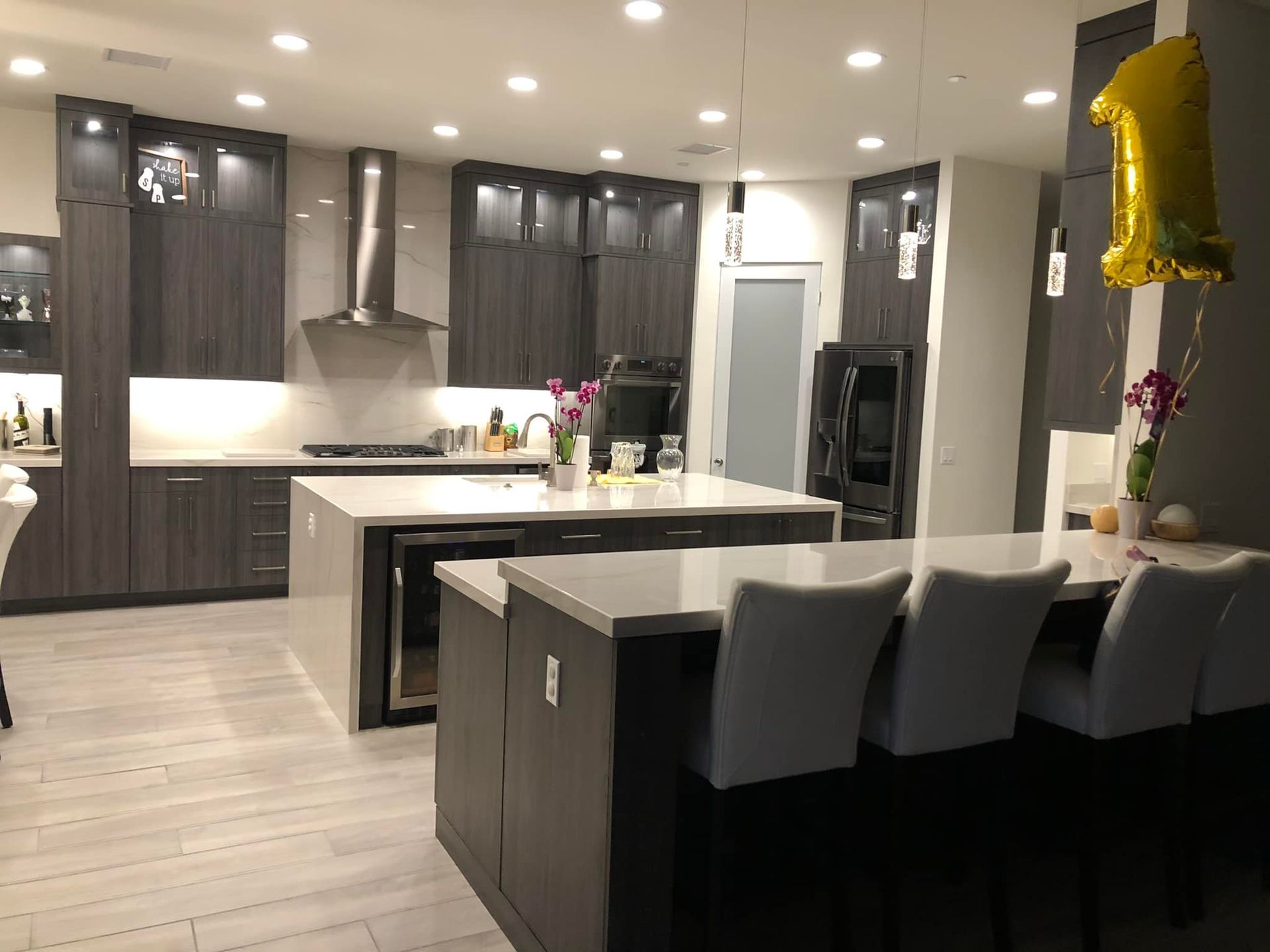 Modern kitchen with dark cabinets, island seating, stainless appliances, and bright recessed lighting