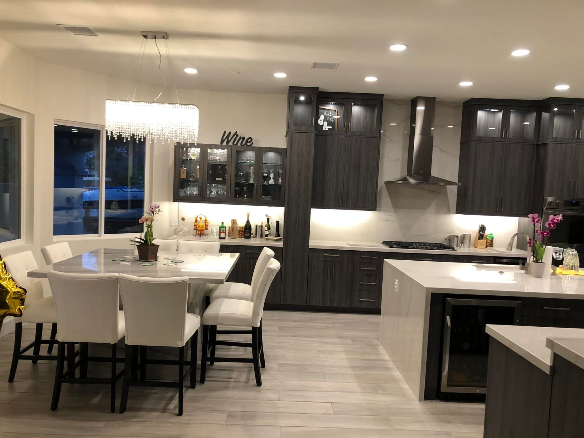 Modern kitchen and dining area with white chairs, dark cabinets, and a large island