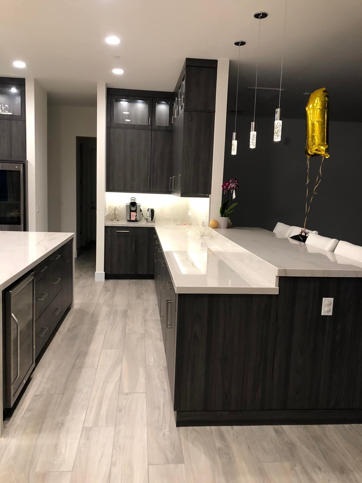 Modern open-plan kitchen with dark cabinets, white island, pendant lights, and gray flooring