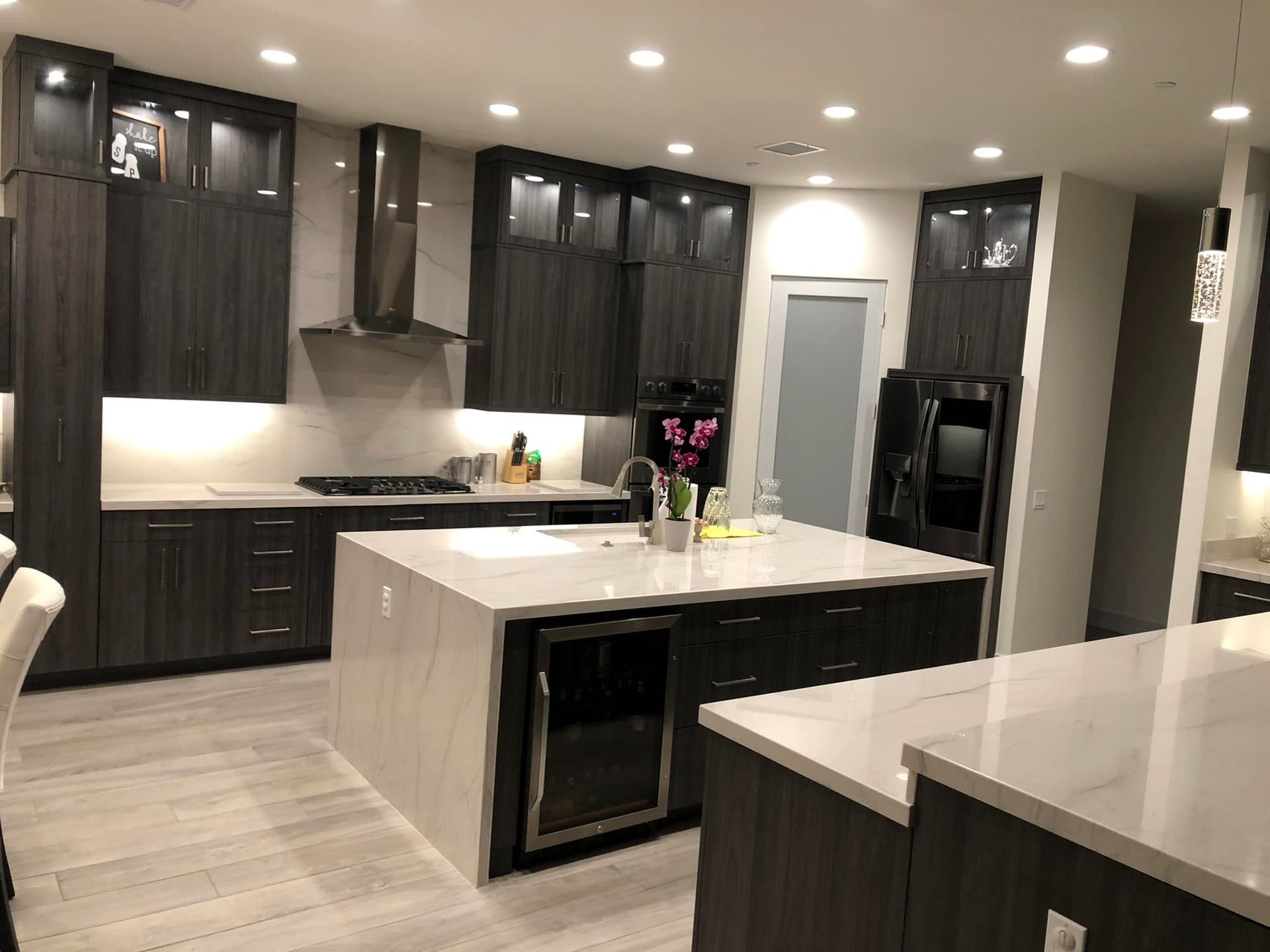 Modern kitchen with dark cabinets, white island countertops, and recessed ceiling lights