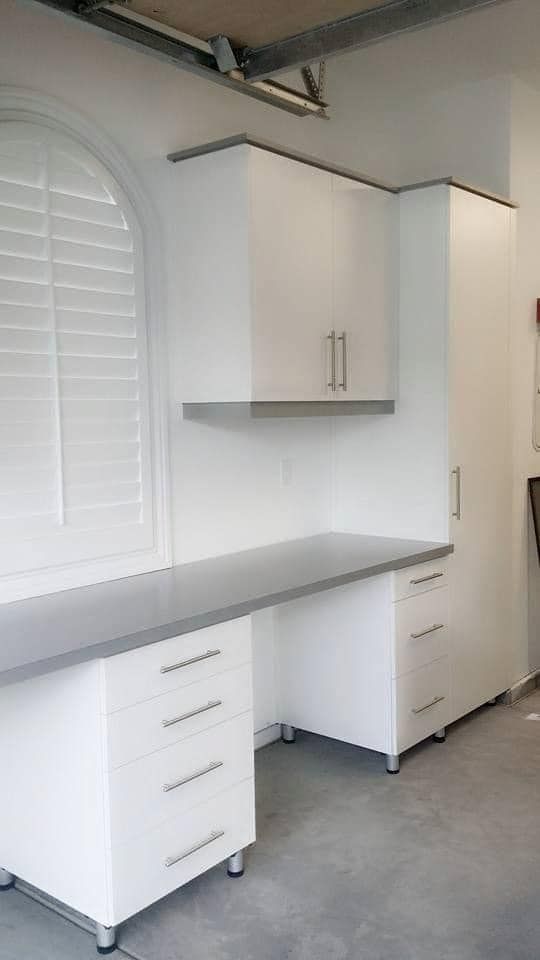Built-in white desk with cabinets and gray countertop in a bright room
