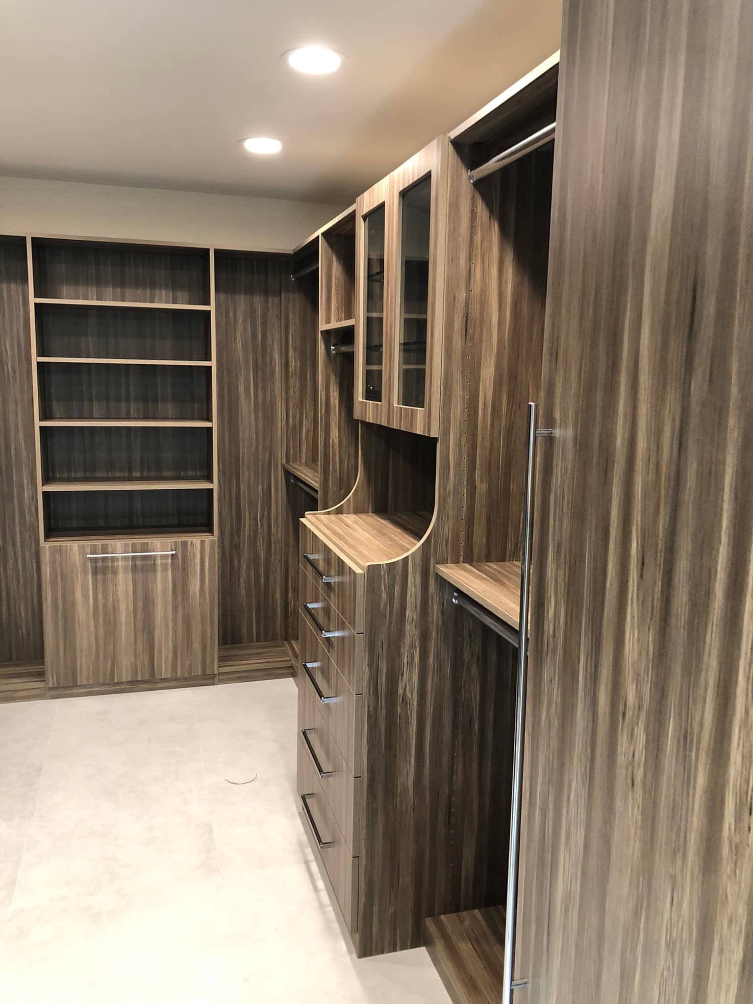 Built-in walk-in closet with wood-grain shelves, drawers, and hanging space under recessed ceiling lights