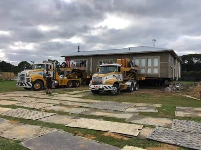 Two yellow construction trucks parked outside a small house on a cloudy day