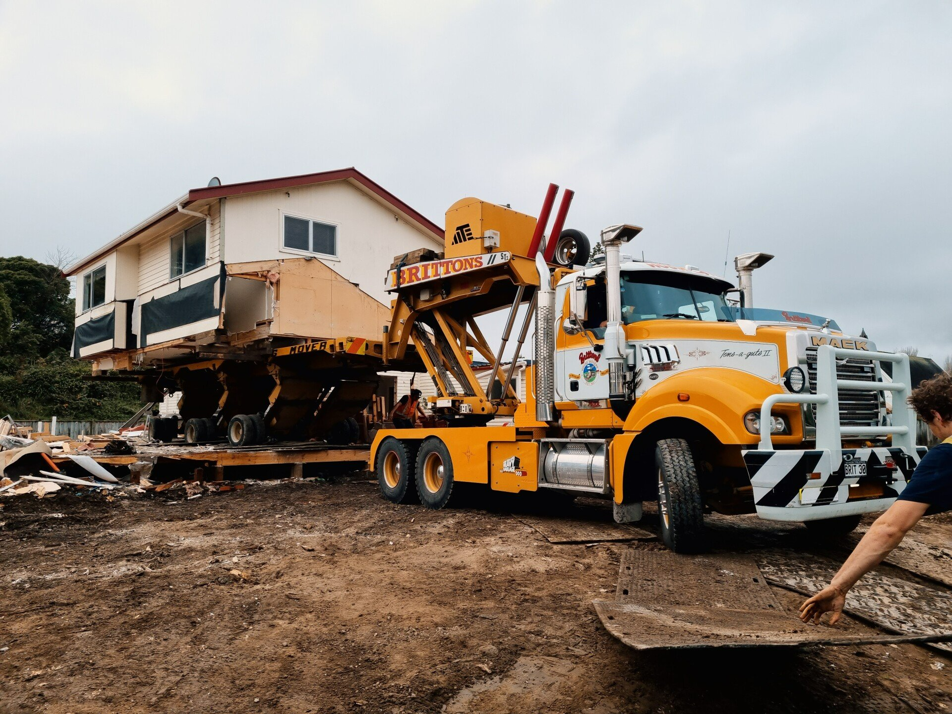 Yellow tow truck lifting a house from muddy ground at a construction site