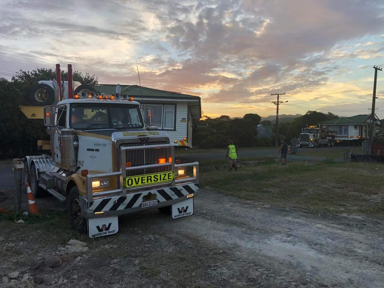 Tow truck parked on a gravel road at sunset with a person in a hi-vis vest nearby