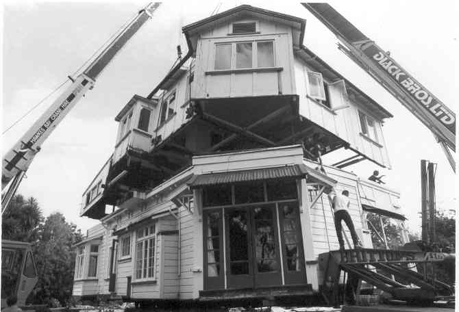 Workers lifting a house with cranes during relocation, black-and-white scene