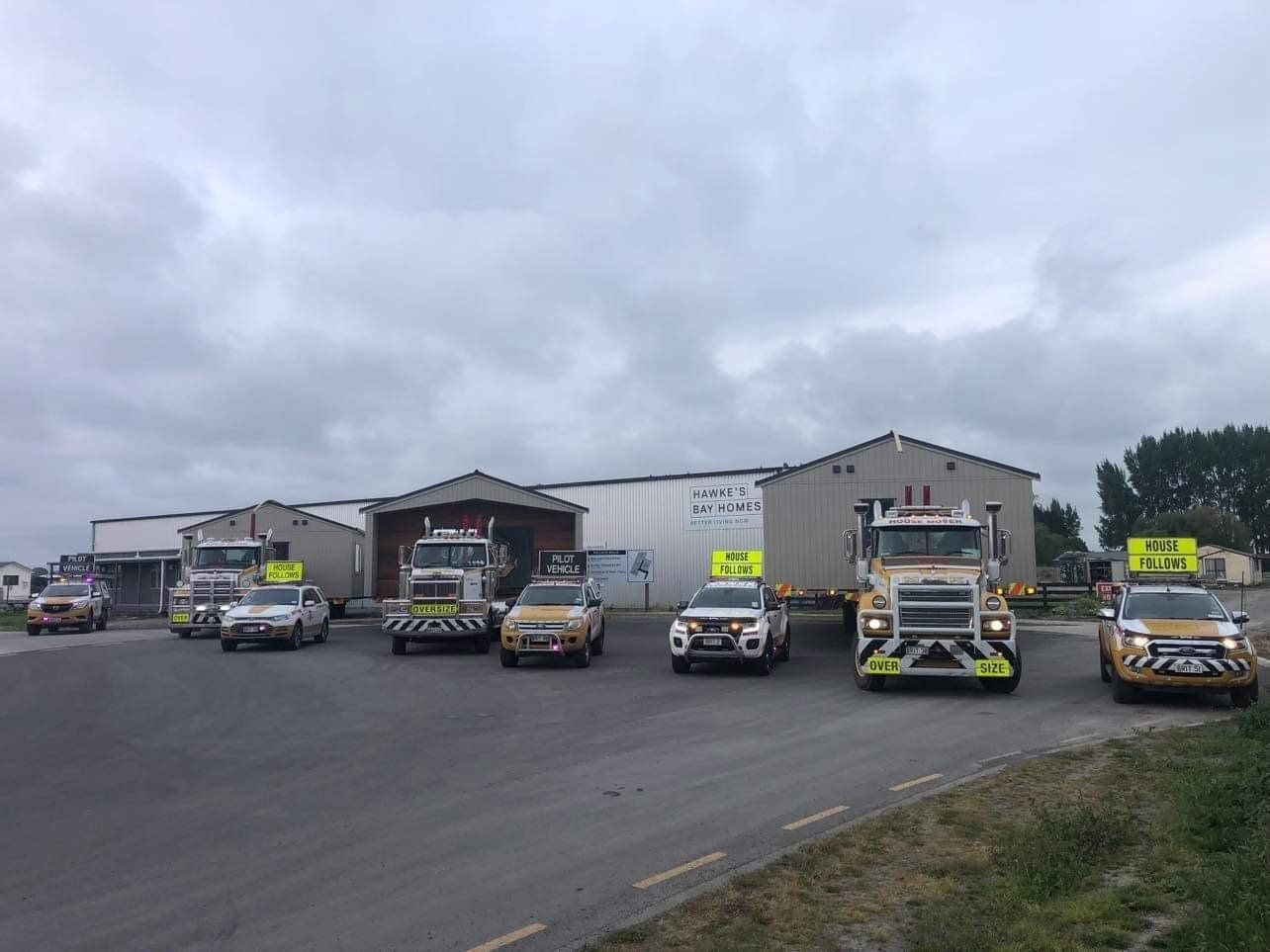 Fleet of utility trucks parked outside warehouse buildings under a cloudy sky.