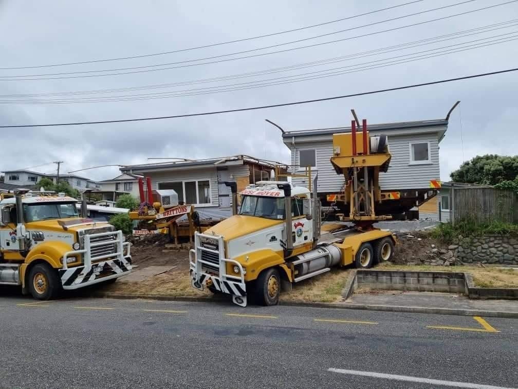 Two yellow utility trucks parked outside houses with a roadside work platform