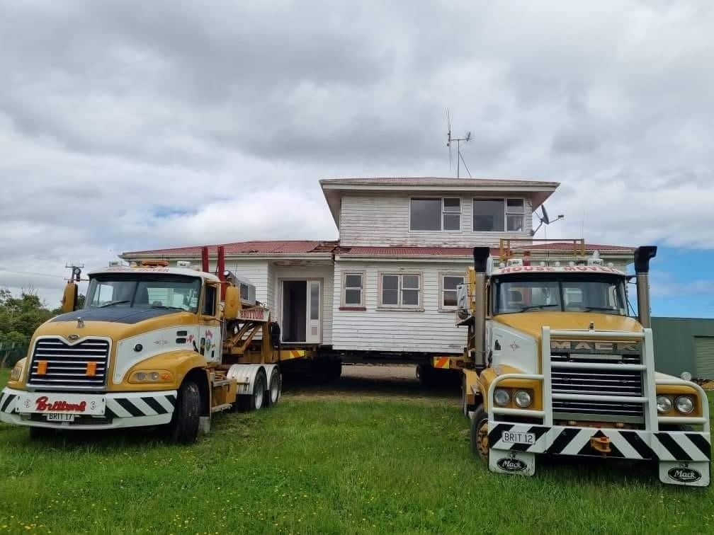 Two yellow tow trucks flanking a white two-story building on grass under cloudy skies