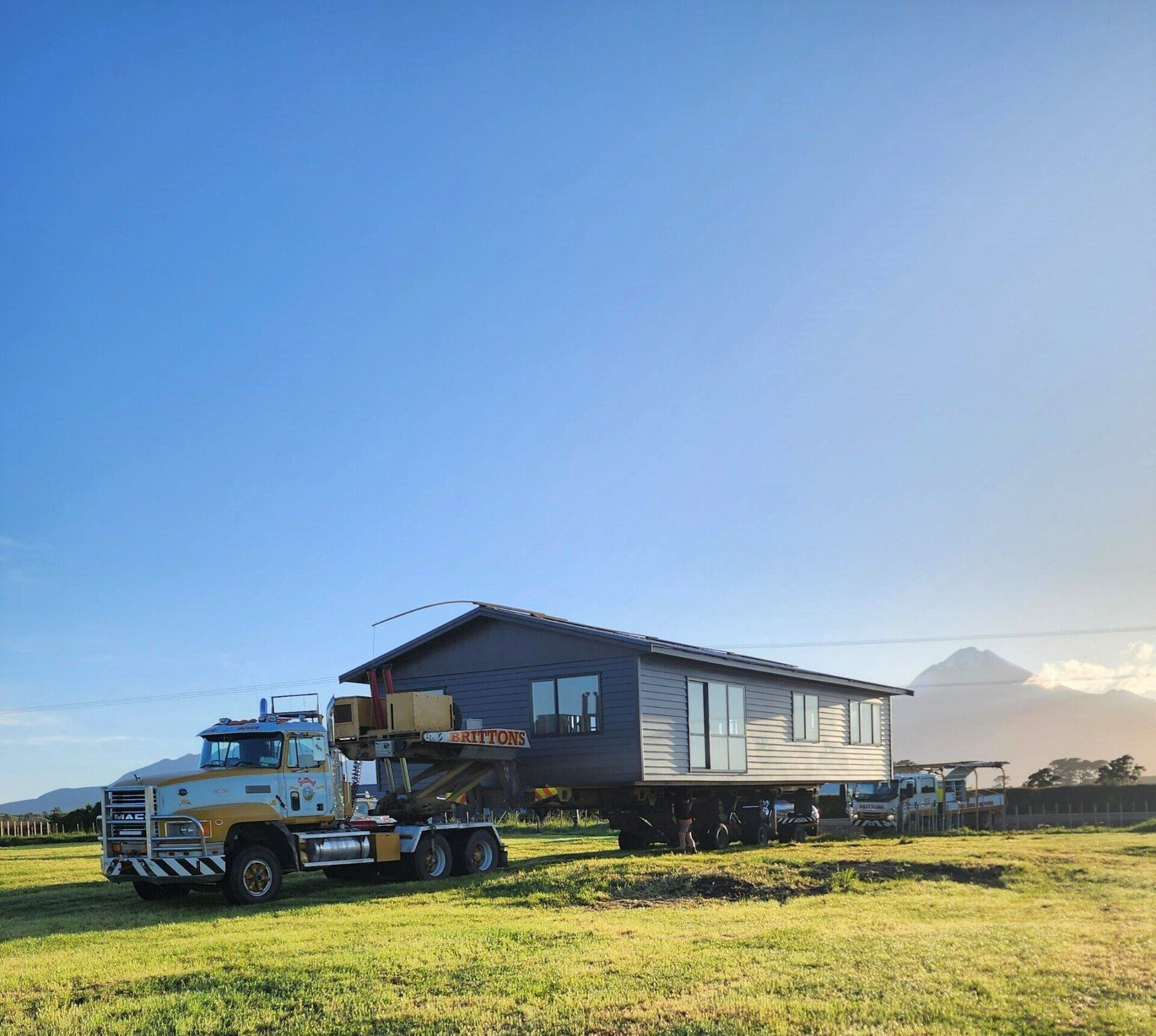 Truck hauling a house on grassland under a clear blue sky