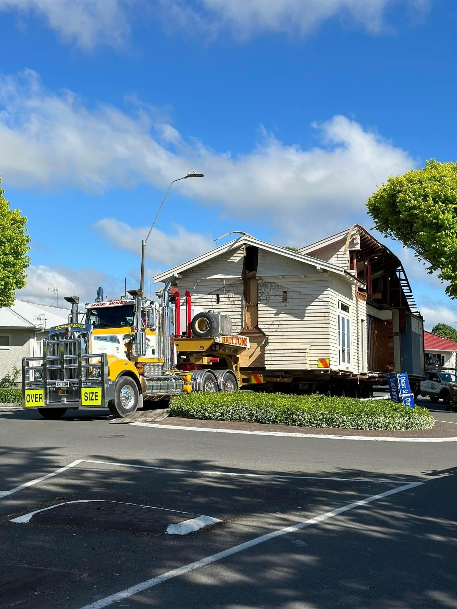 Yellow tow truck outside a damaged house with debris, under a blue sky with clouds
