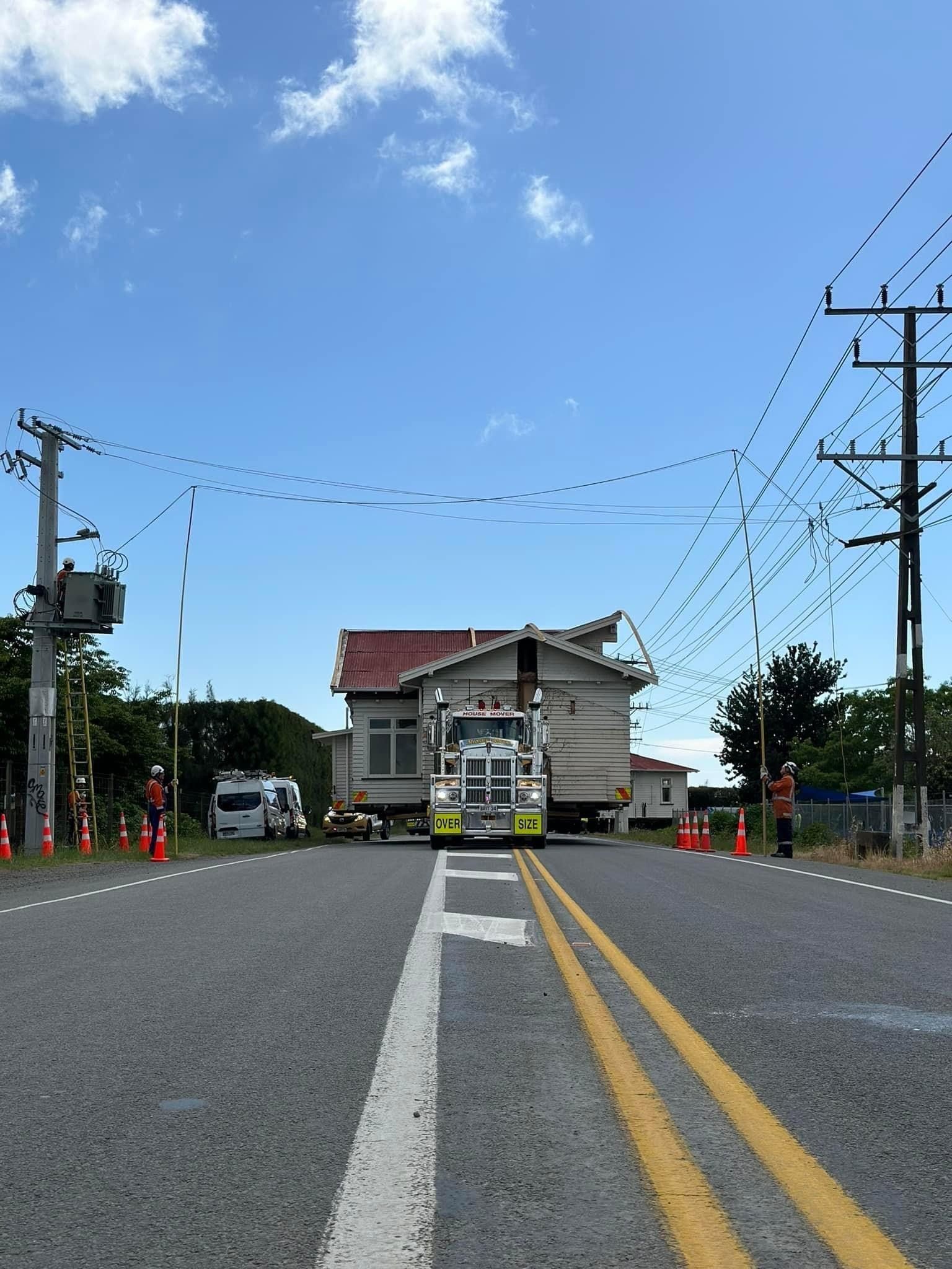 Empty road leading to a small building under a blue sky, with utility poles and road markings.