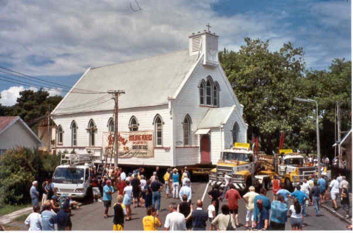Crowd outside a white church at a street festival, with tents and trees under a cloudy sky
