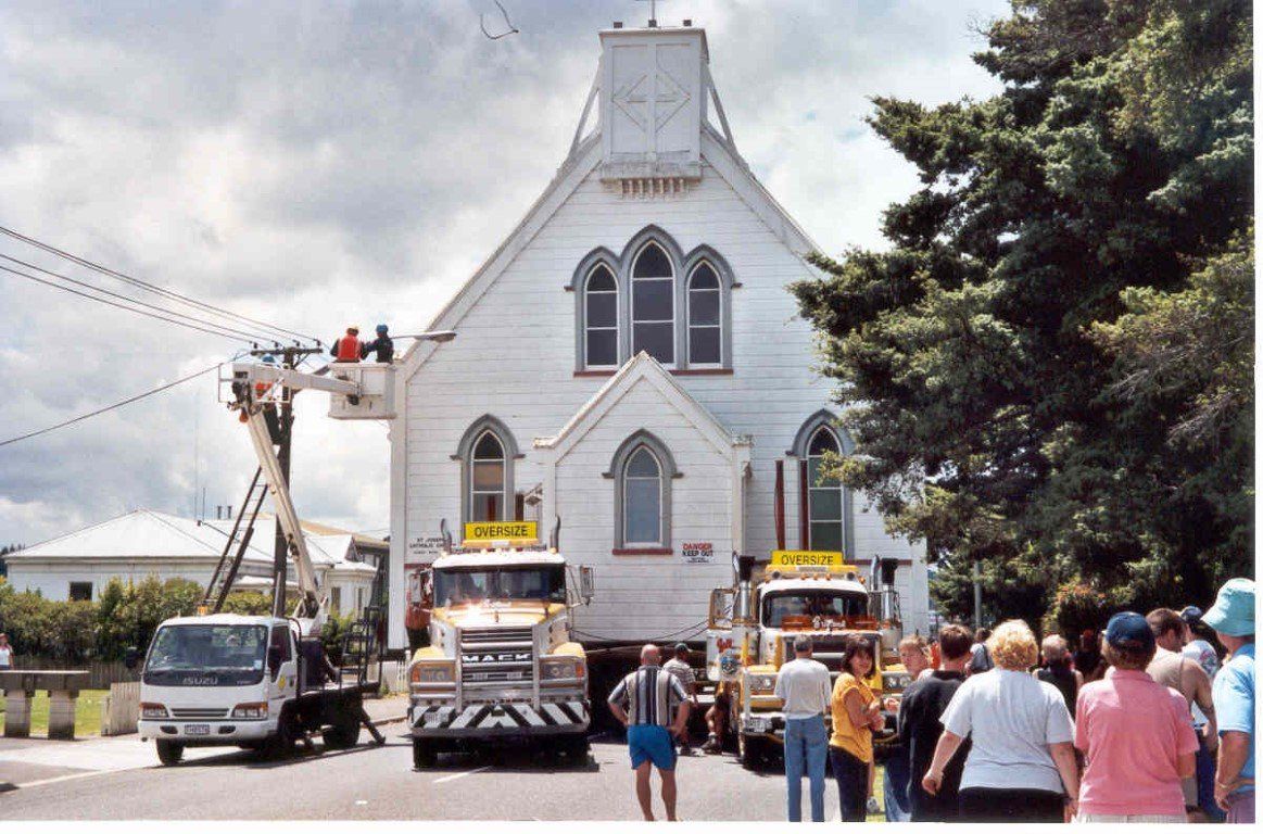 People gathered outside a white church while trucks and a lift support workers on the front façade.