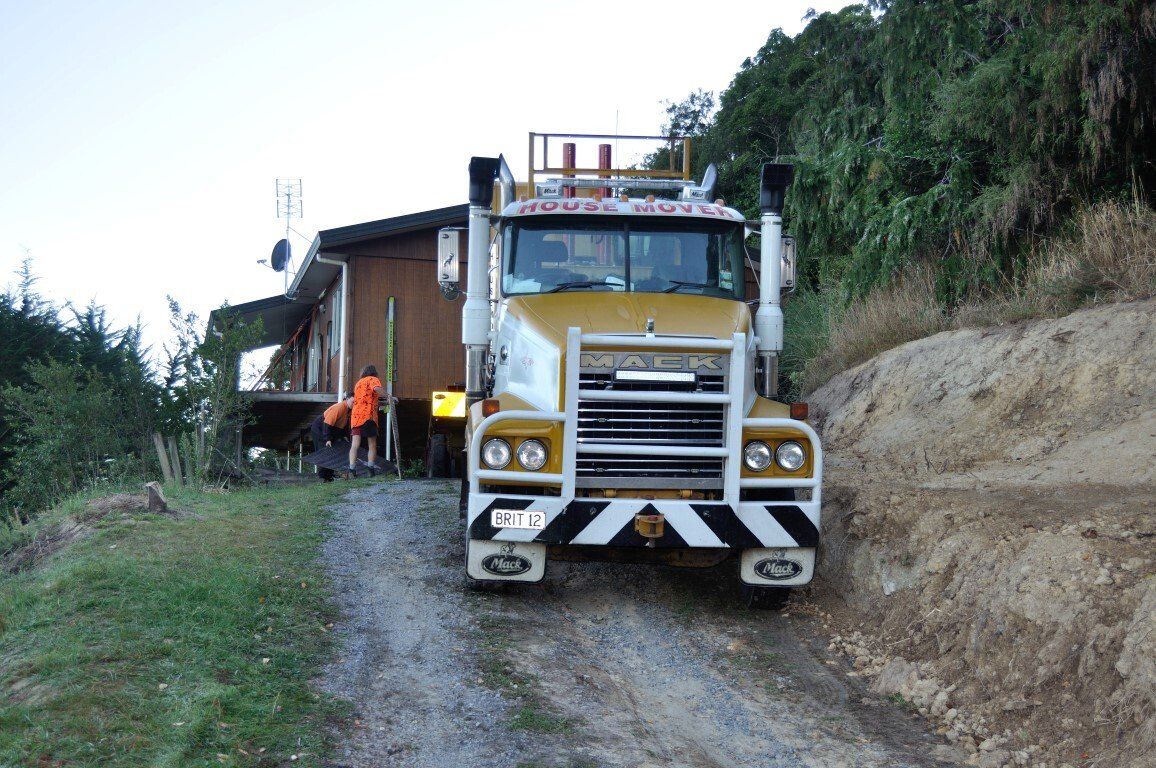 Yellow dump truck on a narrow dirt road beside a hillside, with workers nearby.