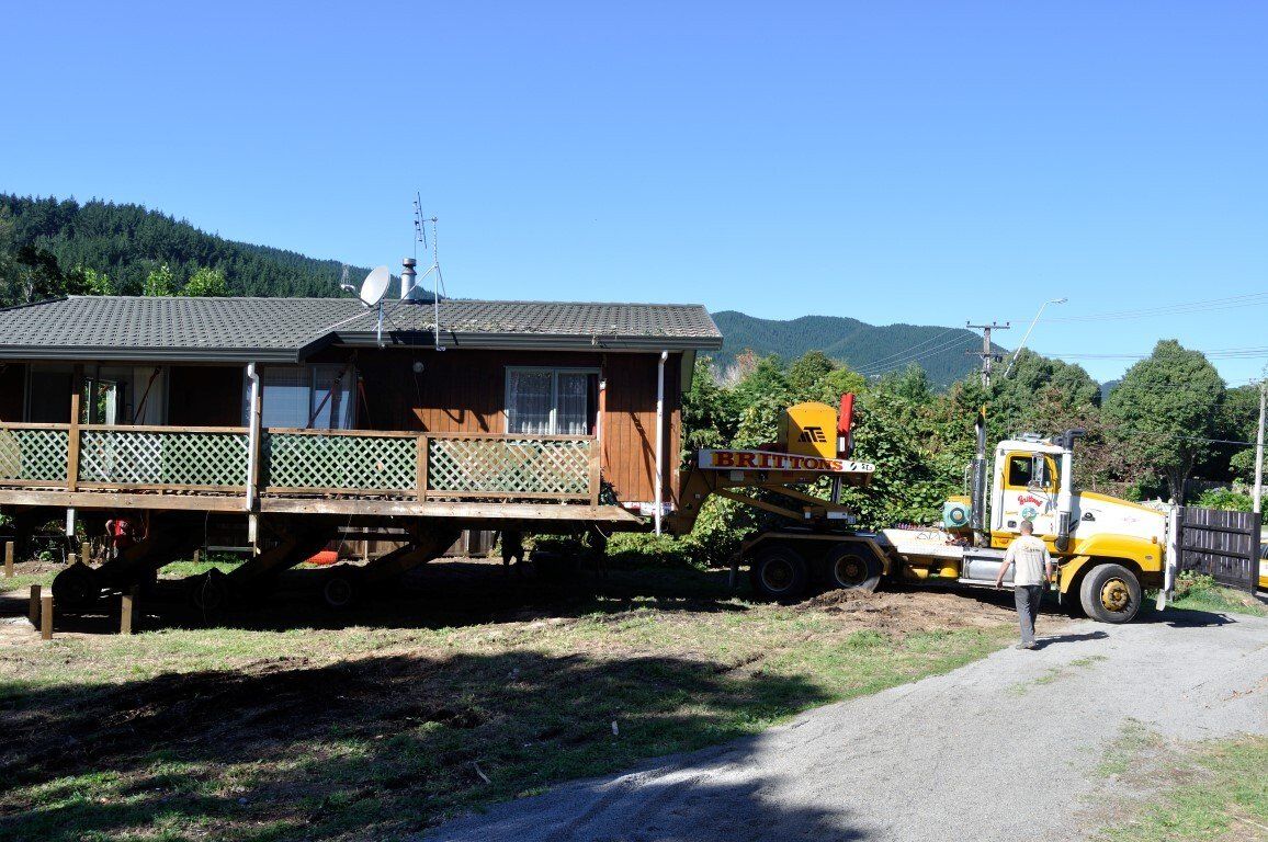 Yellow truck hauling a cabin beside a dirt road in a rural mountain setting