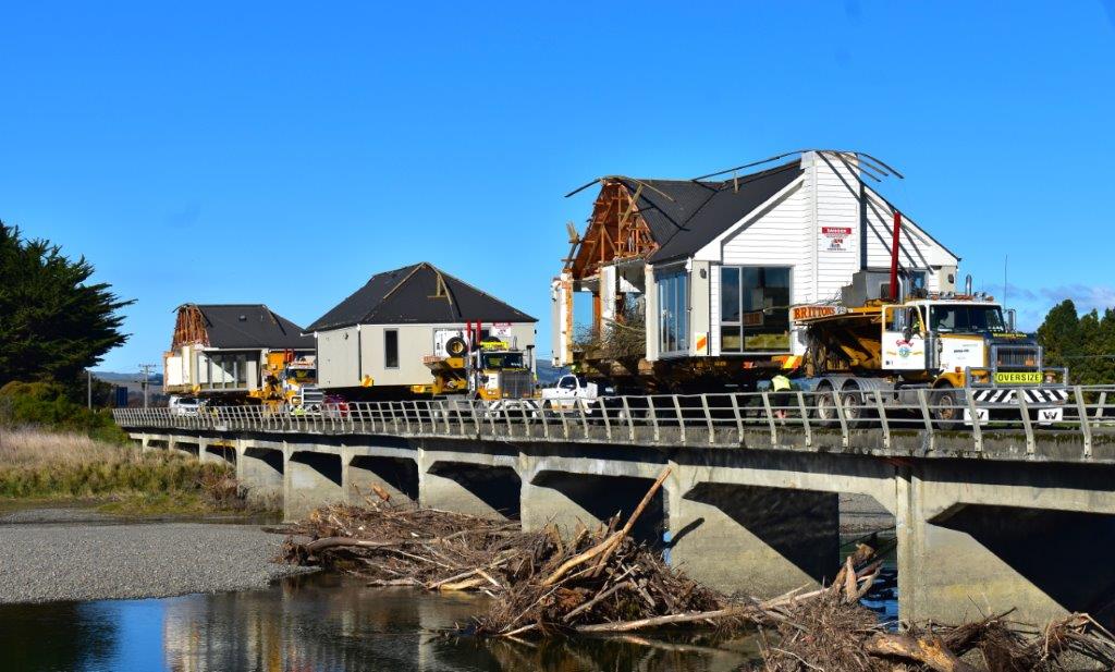 Canal-side houses under construction beside a bridge, with water and a clear blue sky.