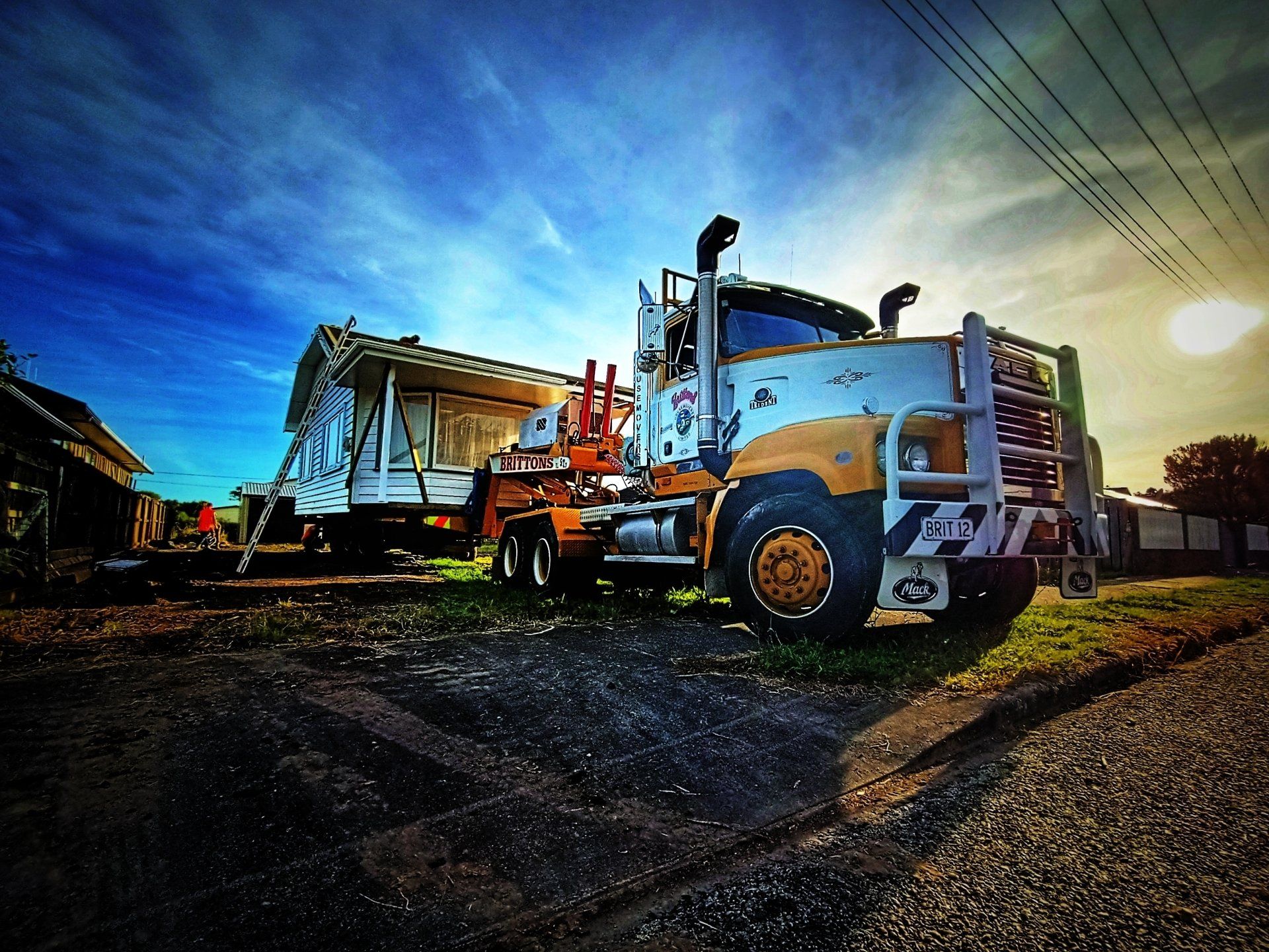 Orange construction trucks on a road at sunset, with a blue sky and power lines overhead