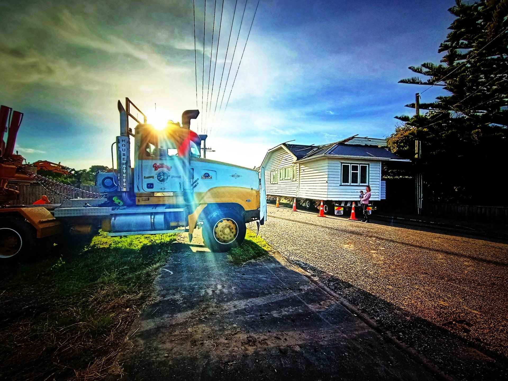 Blue tow truck lifting a white van on a gravel road at sunset
