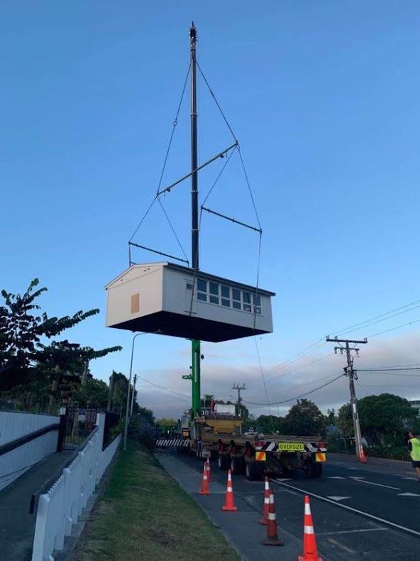 House lifted by crane beside road with orange cones and utility poles at dusk