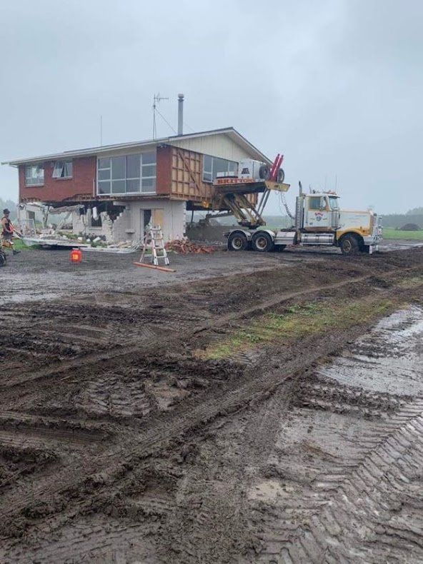 House being lifted by a crane beside muddy construction site on a cloudy day