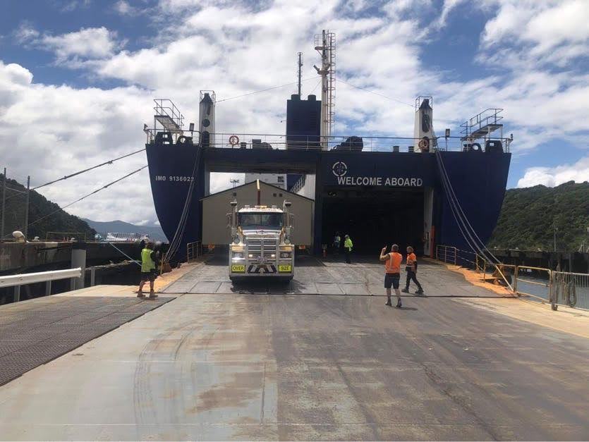 Cargo ship loading ramp with truck on a ferry deck, workers nearby, under a cloudy sky