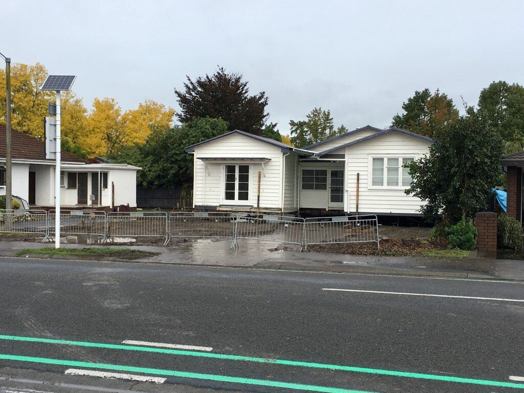 Small white houses behind a metal fence on a rainy street with autumn trees
