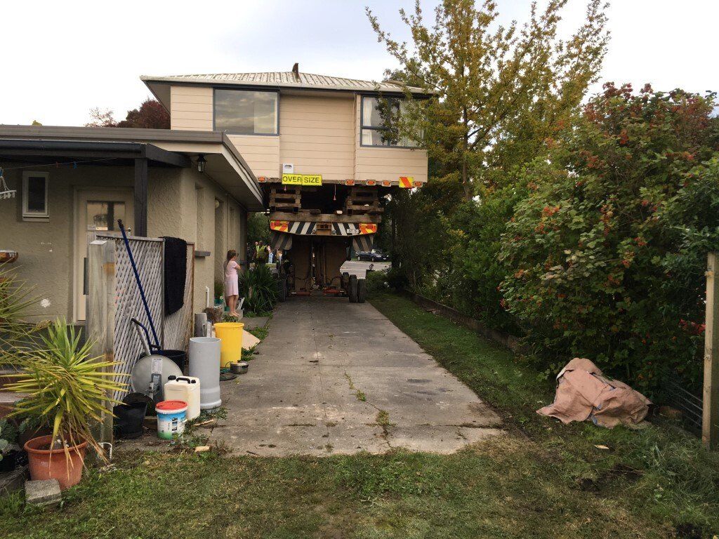 Driveway leading to a house with a carport, plants, and a person standing near the left side.