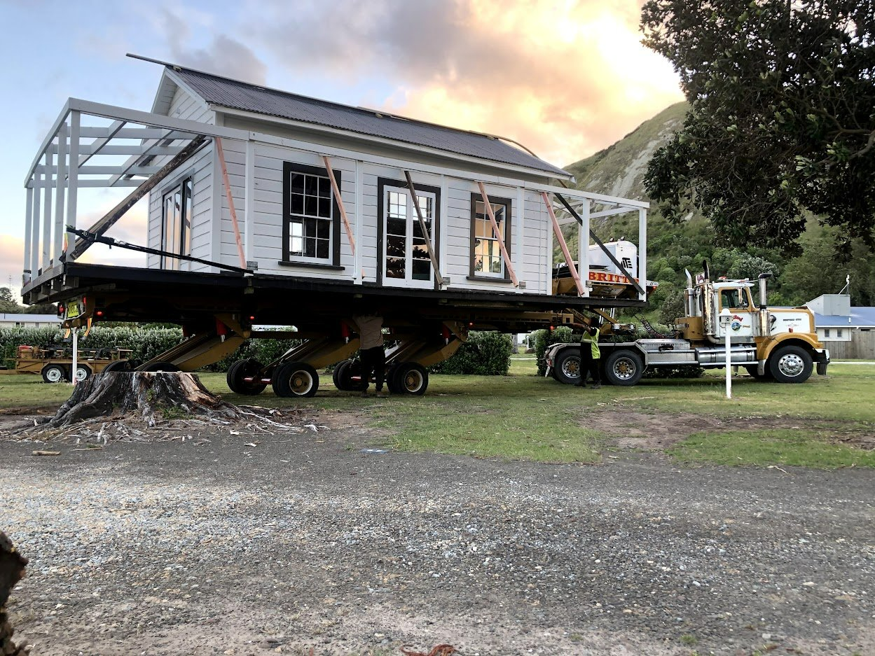 Tiny house on wheels being towed by a truck on gravel, with mountains in the background.