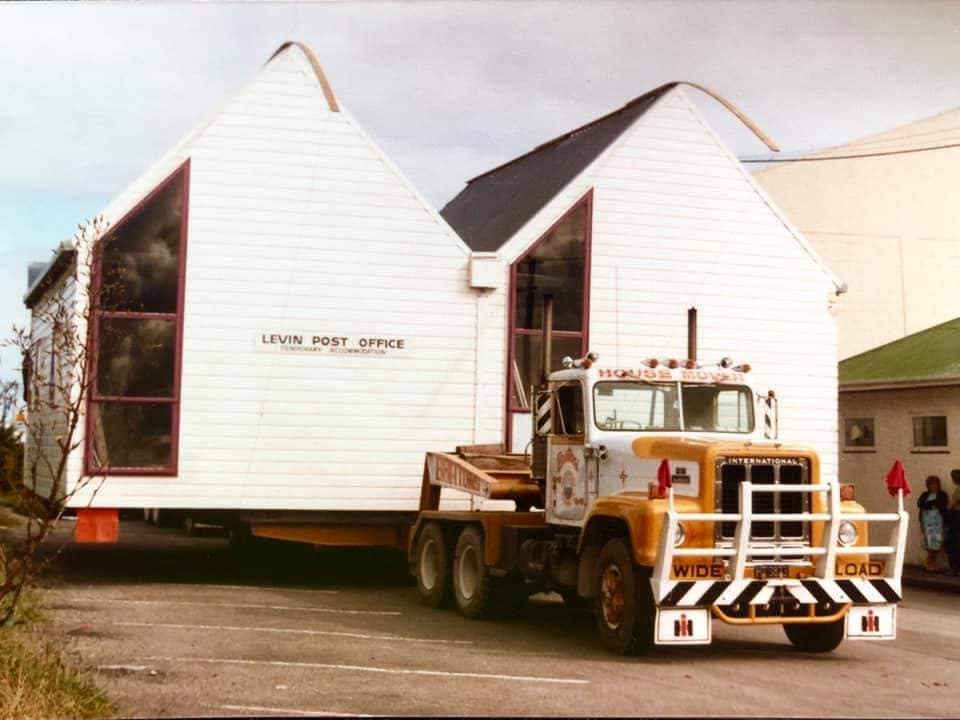 Yellow semi-truck hauling a white house section on a road, with a second house section behind it