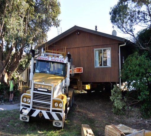 Yellow truck parked in front of a raised wooden house in a wooded yard