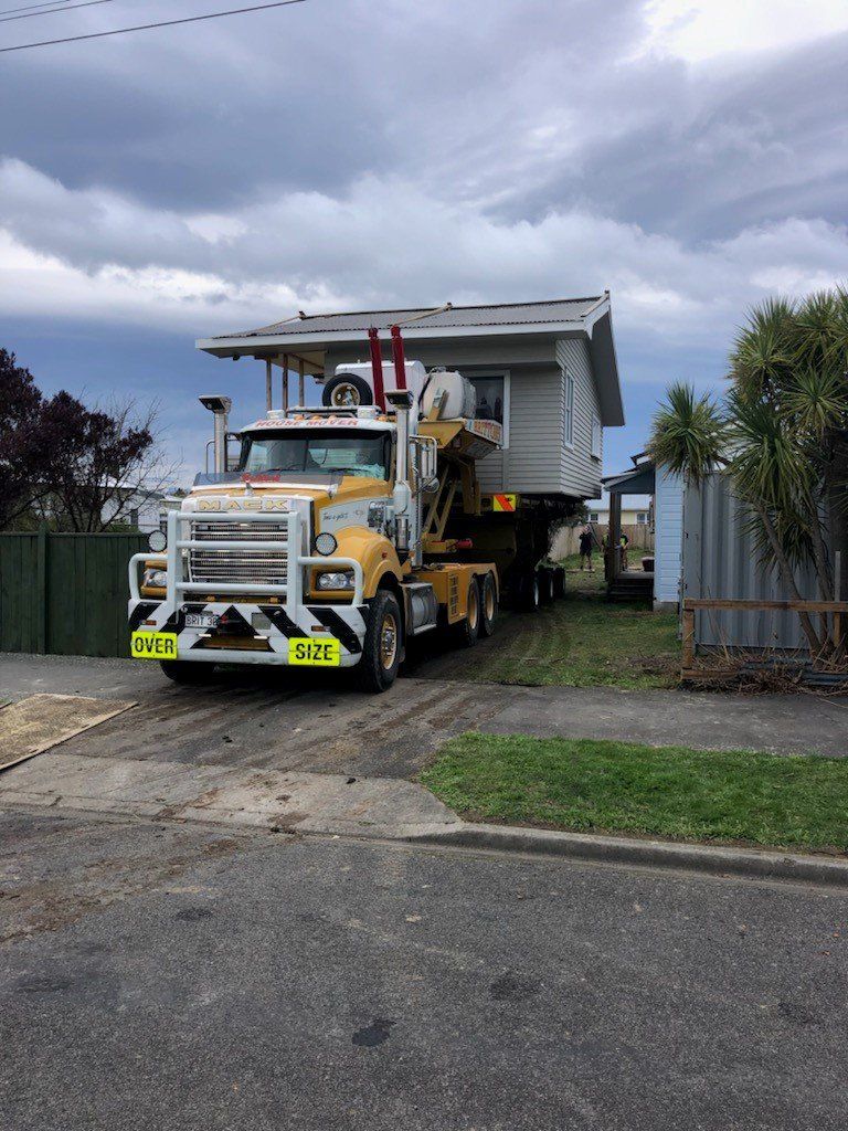 Yellow truck hauling a white trailer through a residential driveway under cloudy skies.