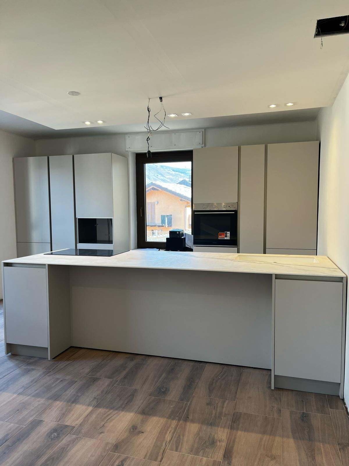 Cucina moderna con un’ampia isola, mobili bianchi e pavimento effetto legno