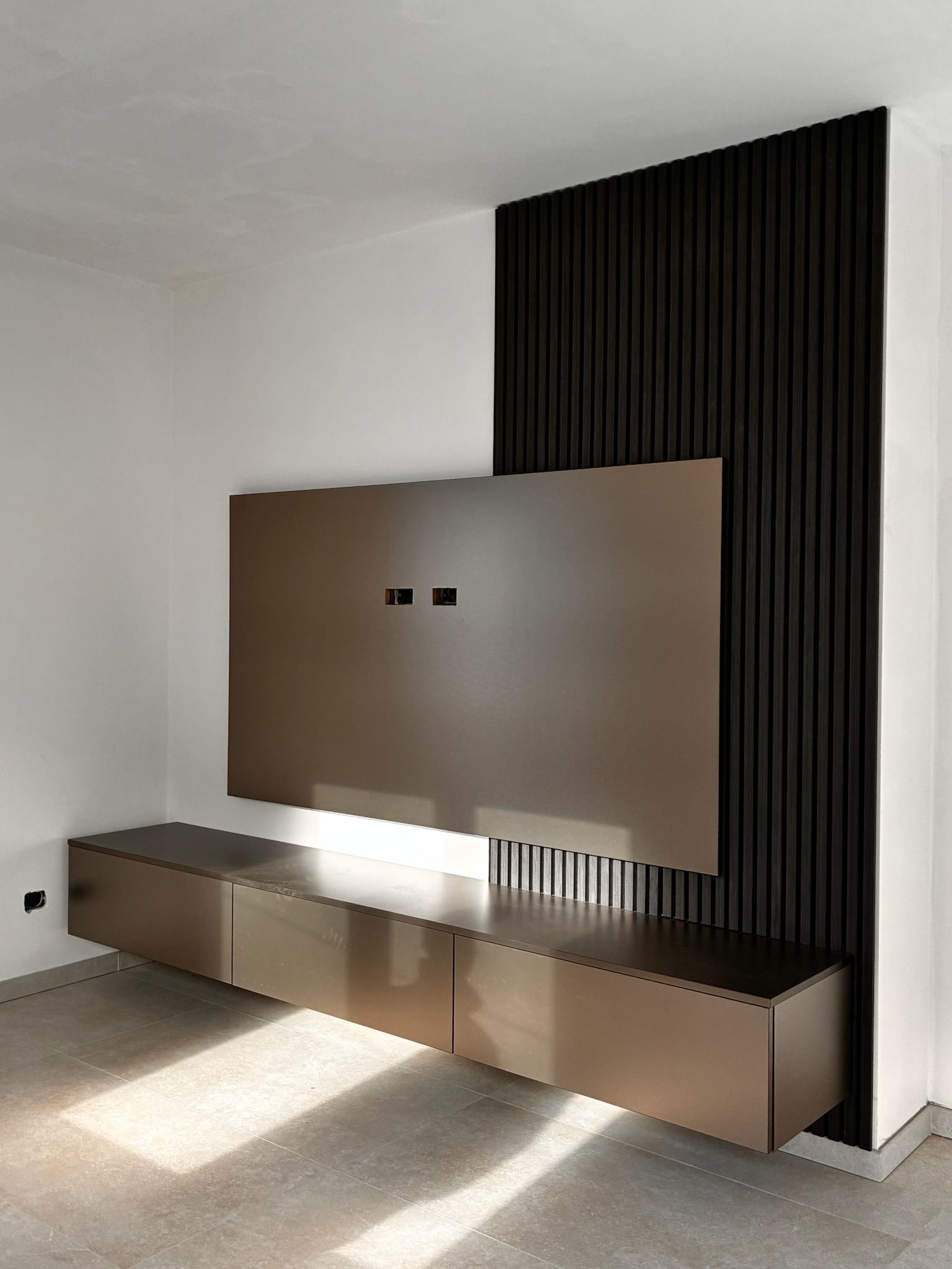 Soggiorno moderno e minimalista con pannello TV a parete, mobili bassi lunghi e luce del sole sul pavimento