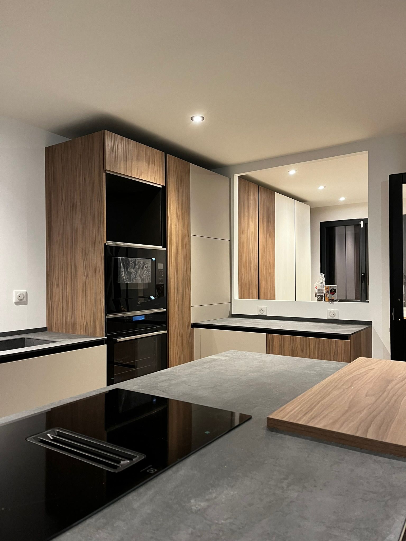 Cucina moderna con mobili in legno, elettrodomestici neri e piano di lavoro grigio, illuminata da calde luci incassate a soffitto