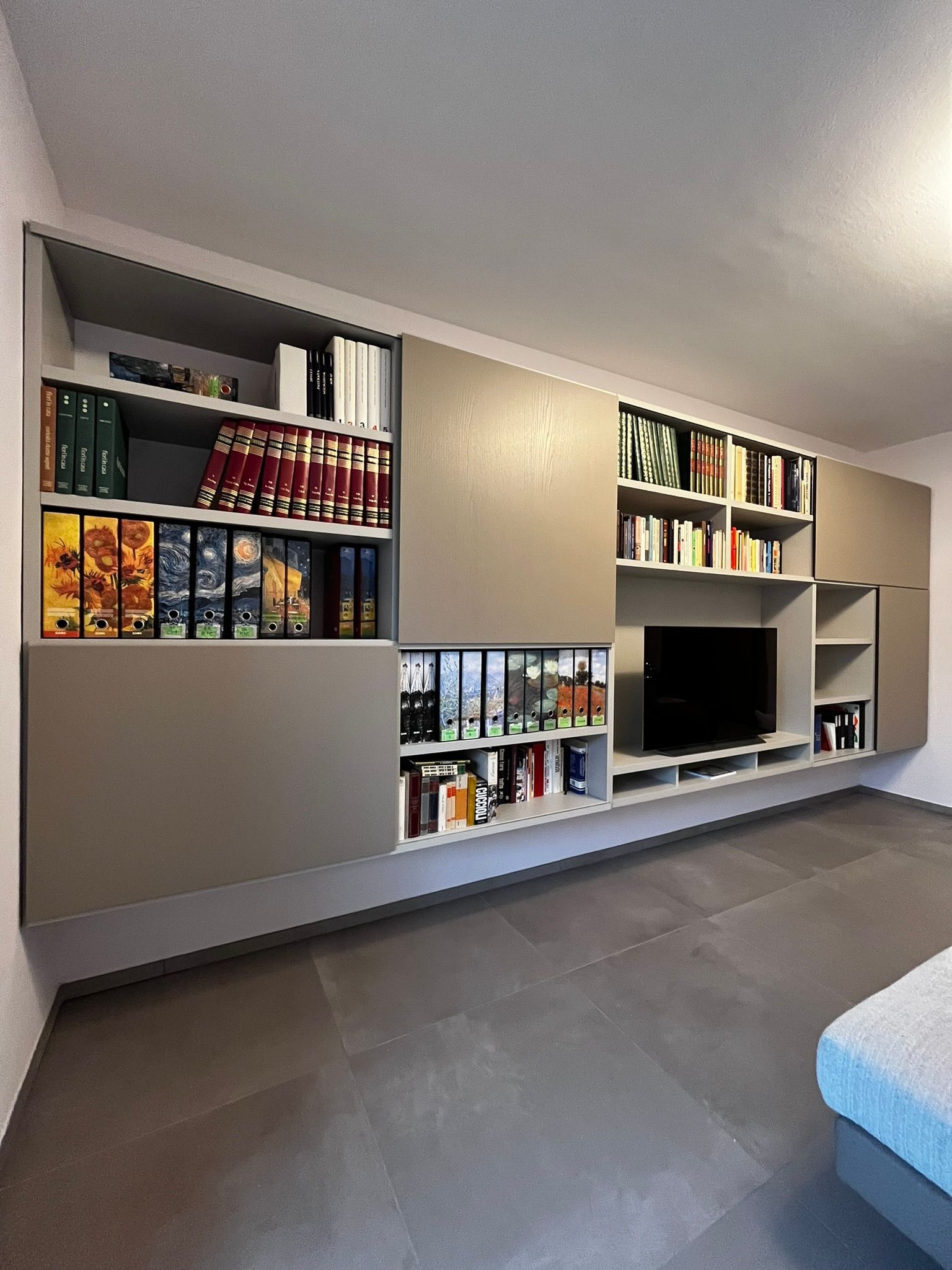 Soggiorno moderno con librerie a muro, libri, una TV e pavimento grigio