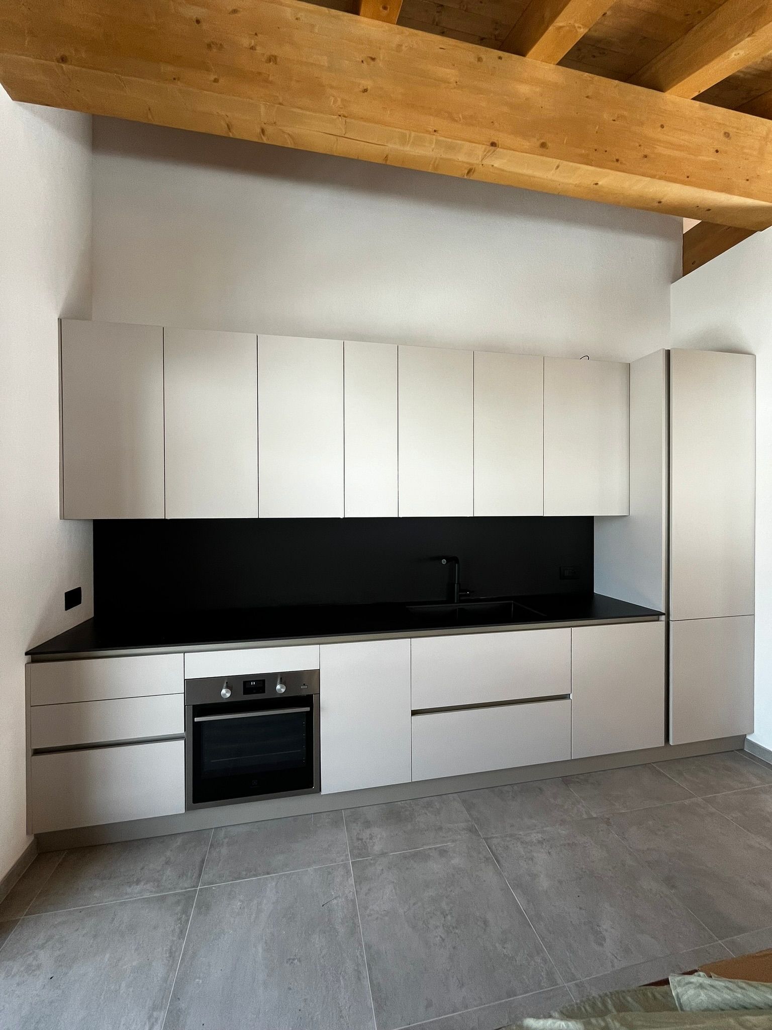 Cucina moderna bianca con paraschizzi nero, forno da incasso e travi a vista in legno chiaro